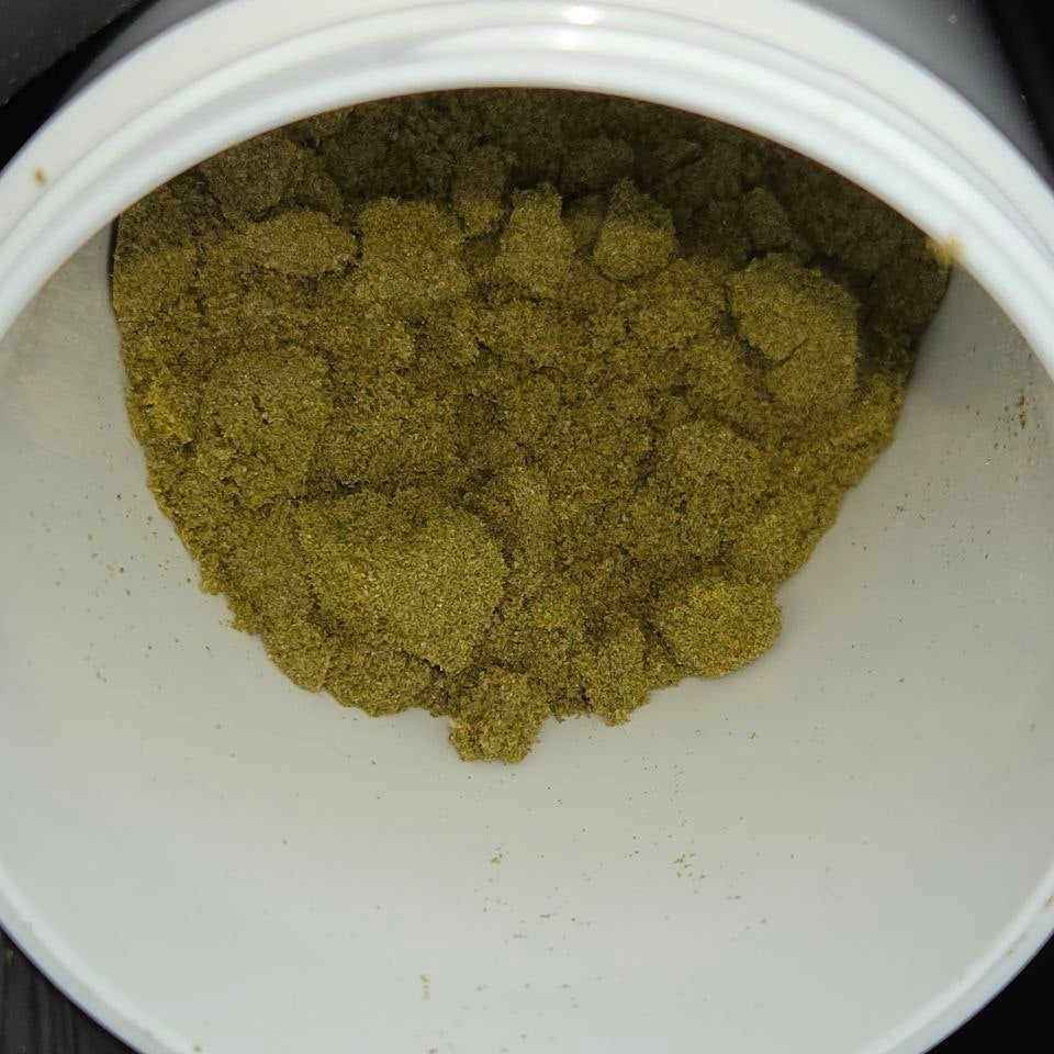 A close-up view of a white plastic jar filled with a textured thca dry sift powder, photographed from inside the container.